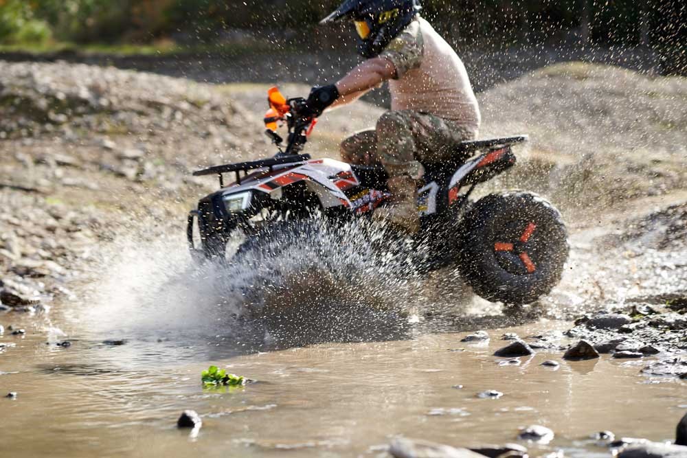 FR125ATV-UT utility quad splashing through a muddy water crossing on wet farm terrain